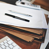 Documentos y carpetas sobre un escritorio, con dos bolígrafos y un teclado al lado